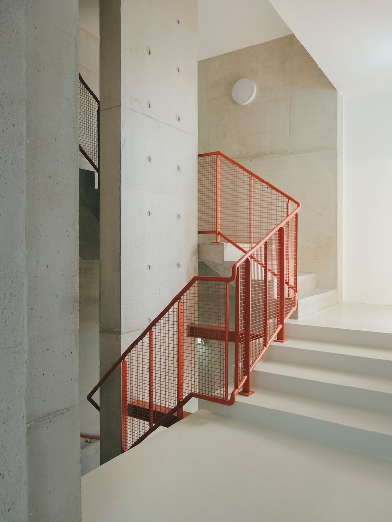Concrete staircase with red-orange mesh railings between cast concrete columns and white walls