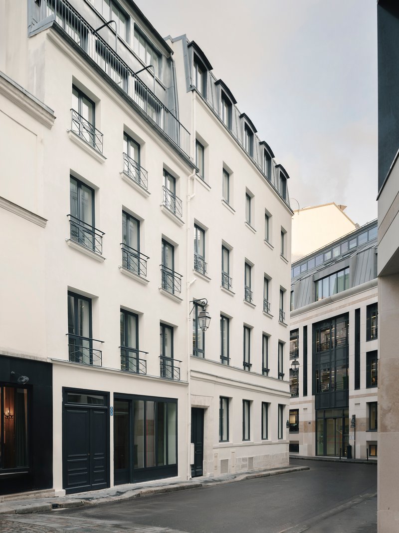 Street view of white stucco facade with rows of metal balconies under an overcast sky