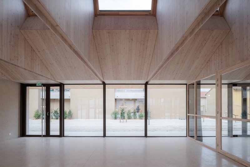 Interior space with exposed timber ceiling beams and full-height glazing overlooking an exterior courtyard
