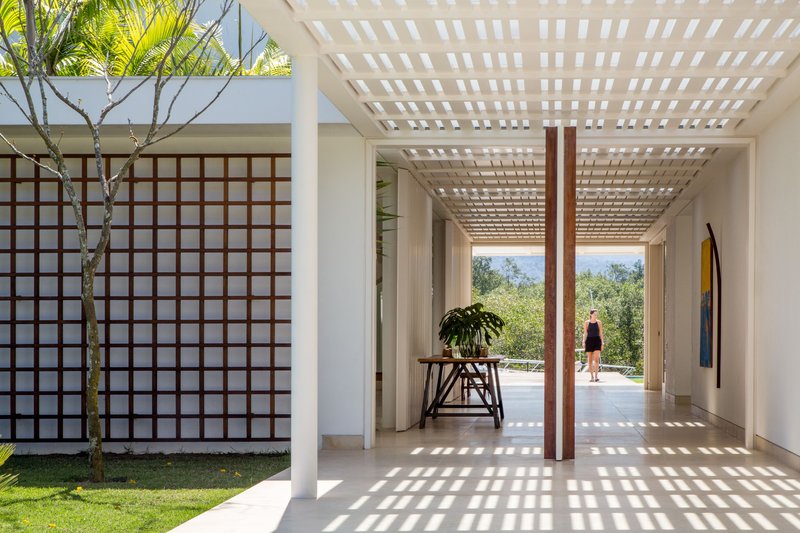 Covered corridor with white pergola casting dappled light beside a gridded wooden screen wall