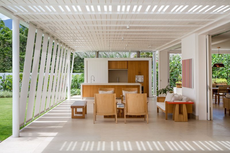 Open dining area beneath a slatted white pergola with wooden furniture and vertical louver screen