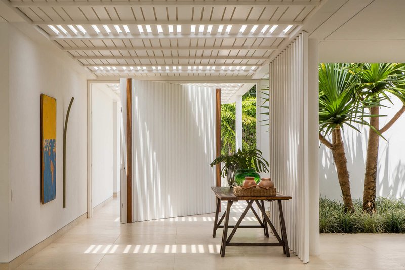 Interior courtyard with slatted timber pergola casting shadows over potted plants and palm trunks