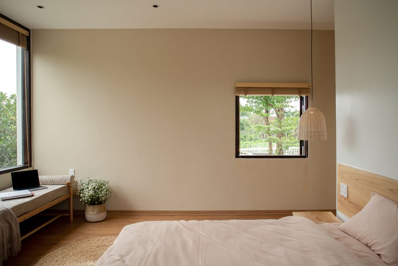 Bedroom with pale walls, timber bed frame, woven pendant light, and window overlooking garden foliage