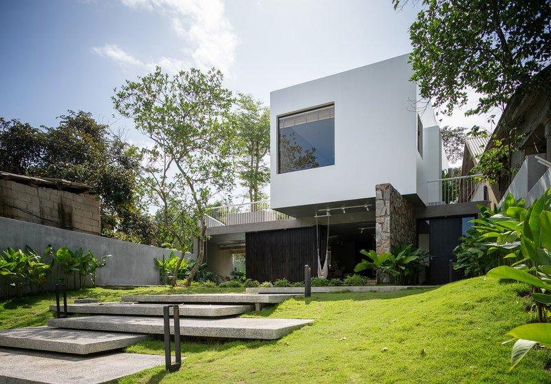 Garden view with wide terrazzo steps ascending through lawn toward the white cubic volume and preserved tree