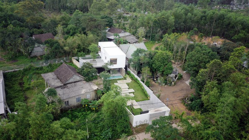 Aerial view showing the white volumes and swimming pool nestled among dense tropical vegetation and neighboring houses