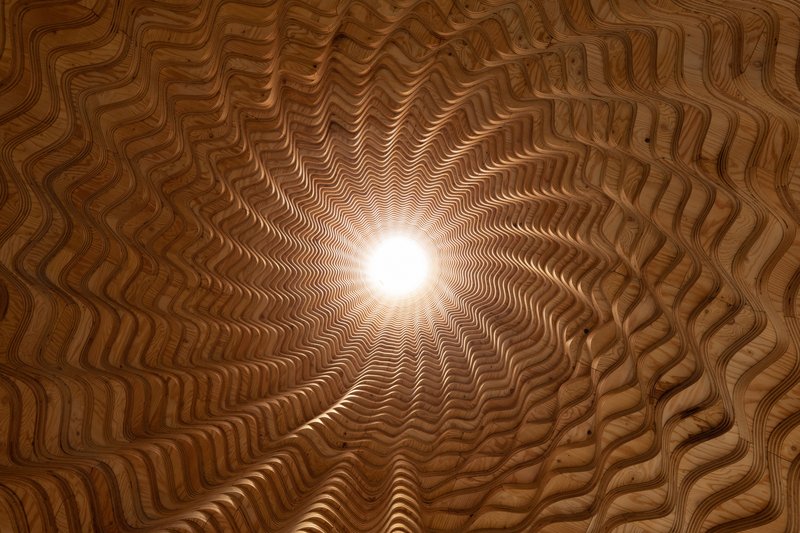 Upward view through ribbed timber oculus with sunlight filtering through the central opening