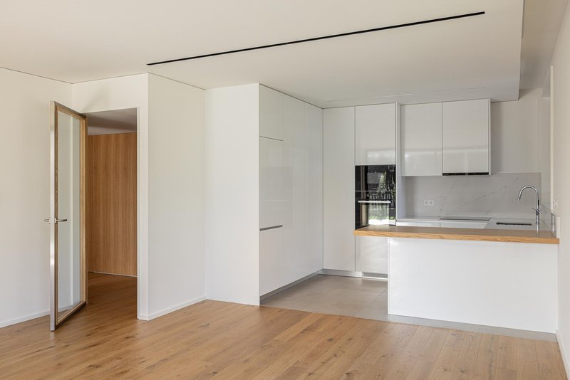 Open-plan kitchen with white cabinetry and oak flooring viewed from the living area