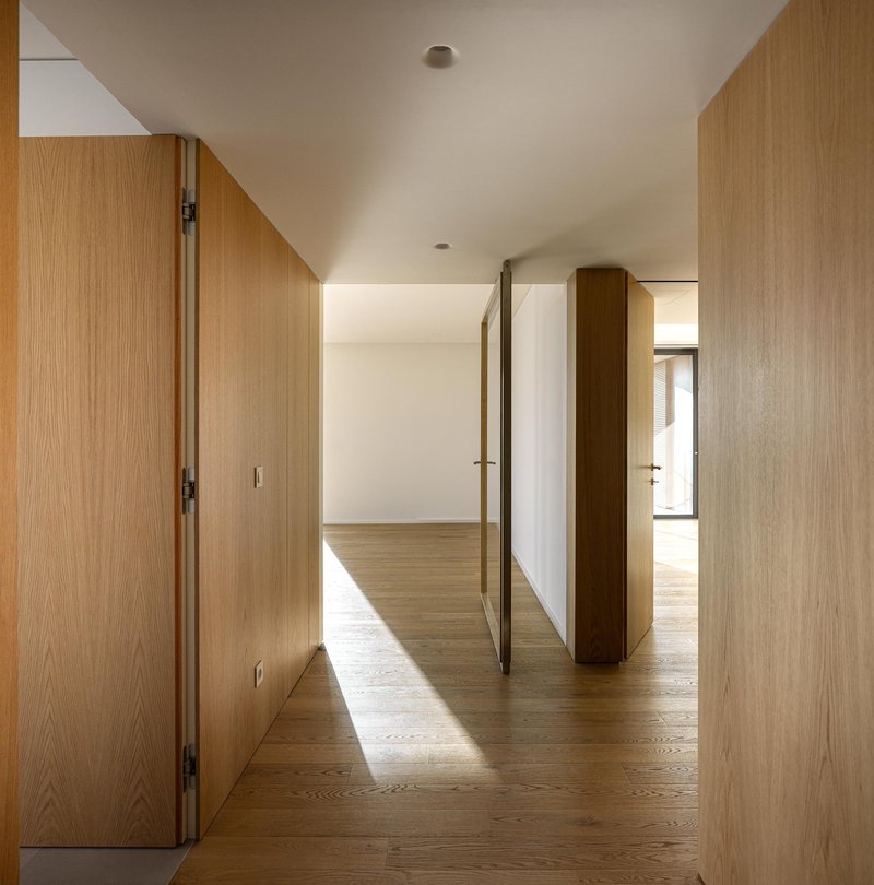 Oak-paneled corridor with pivoting door open to sunlit interior spaces