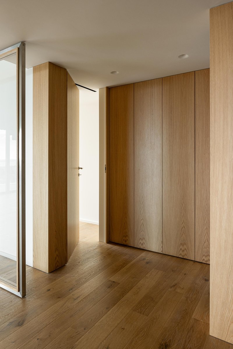 Oak wall panels concealing storage with full-height pivot door ajar