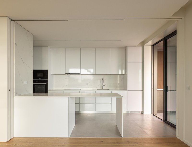 White kitchen with integrated island and marble backsplash opening onto timber flooring in soft natural light