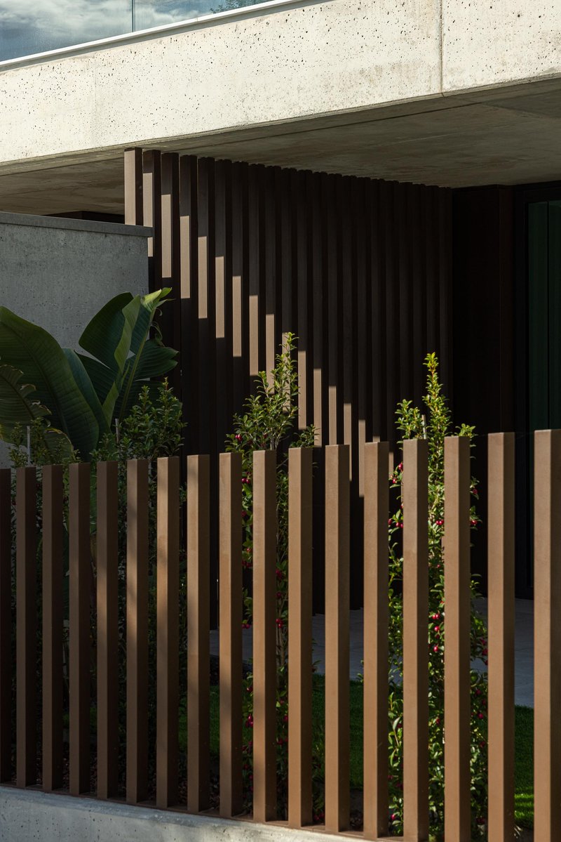Vertical timber slat screen in front of planted bed with tropical foliage beneath concrete overhang