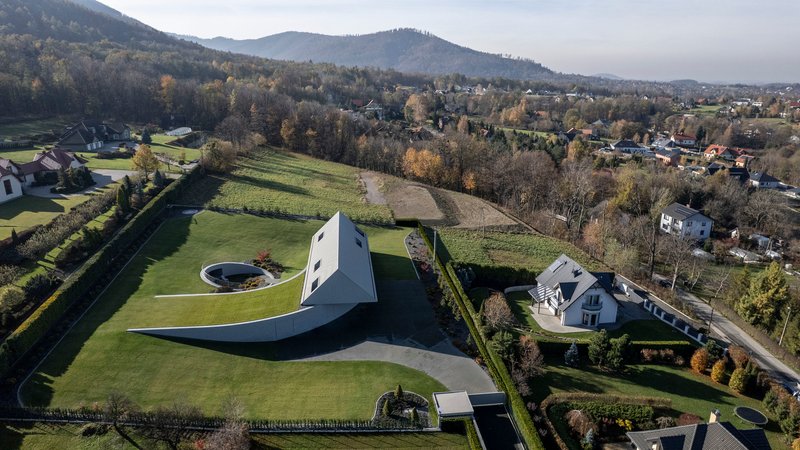 Aerial view showing white gabled house with curved underground extension in terraced landscape