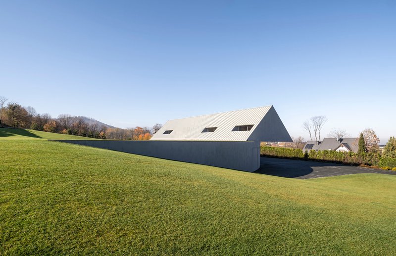 Side elevation showing the ribbed metal roof and dark facade against rolling hills in autumn