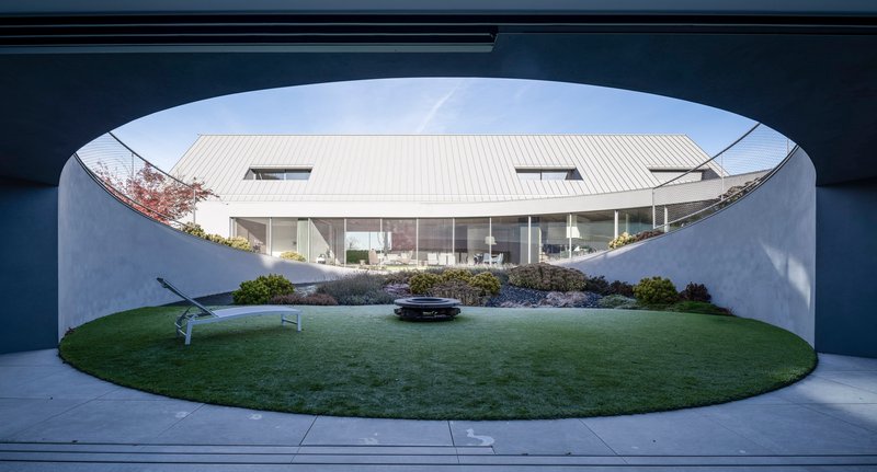 View through arched concrete portal onto glass-walled living space and circular lawn courtyard below