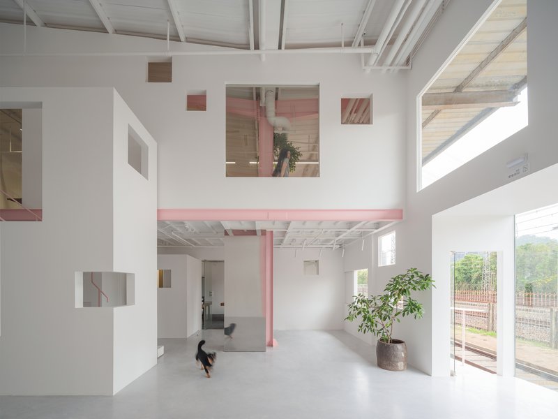 Mezzanine level with pink steel walkway connecting white volumes as a person sits below