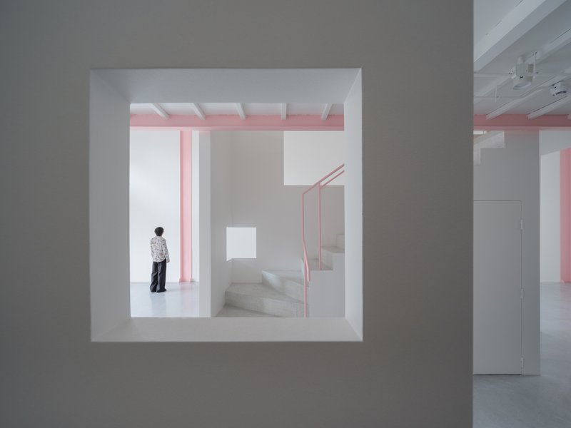 View through a square wall opening showing a person standing near pink steel stairs