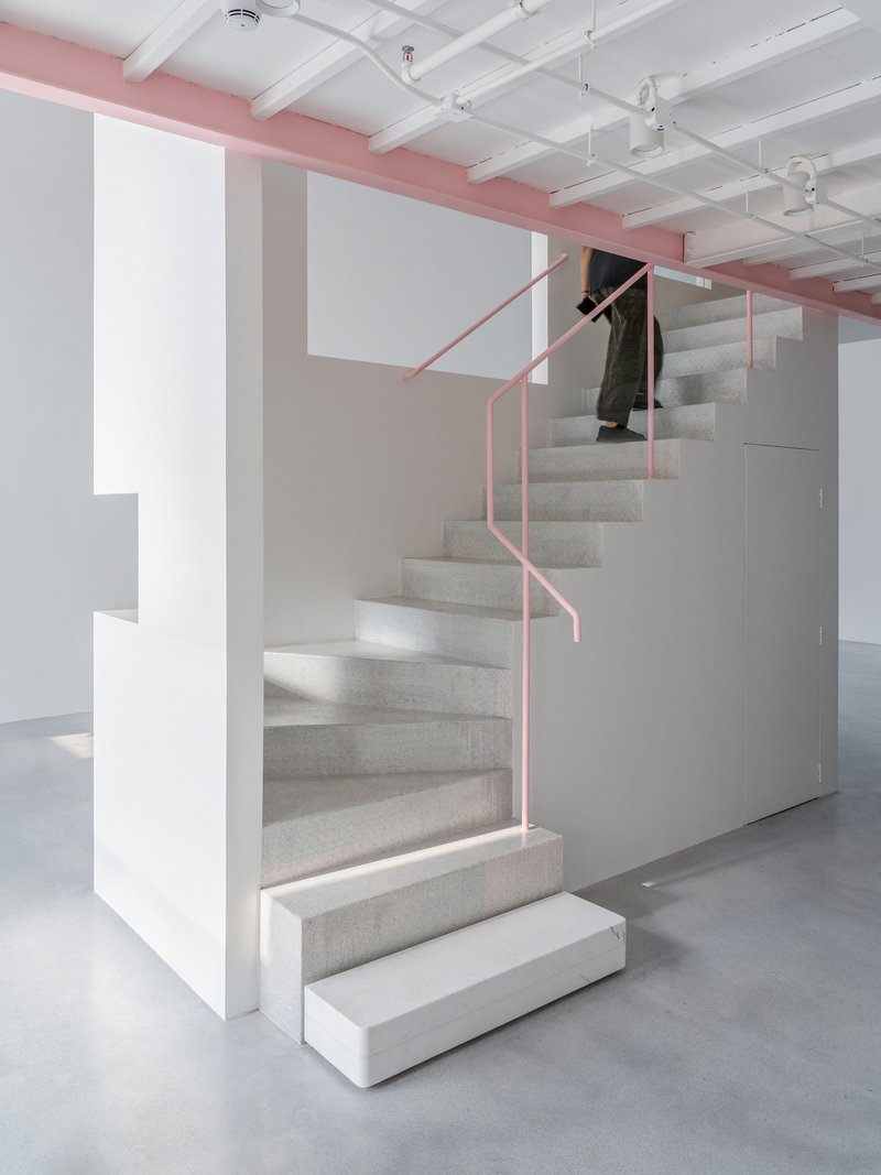 Carpeted staircase with pink tubular steel handrail ascending beneath exposed white coffered ceiling with pink structural beam