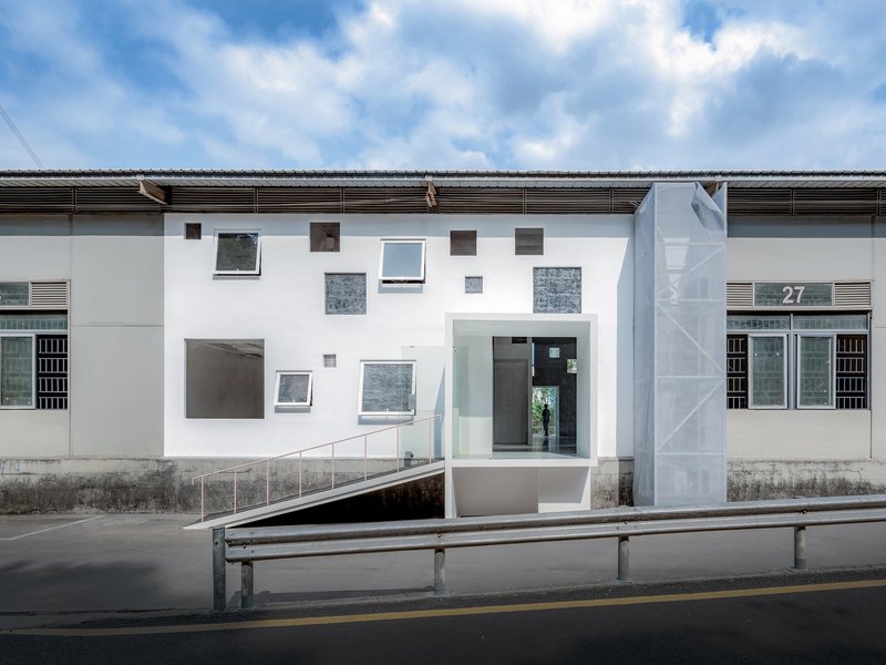Street view of white facade with scattered windows and recessed entrance under cloudy sky