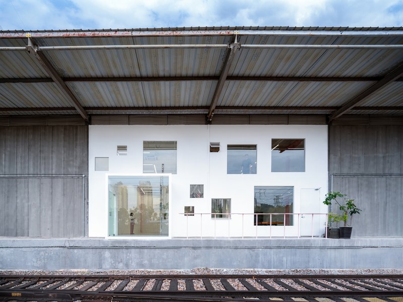 White facade with varied window openings and potted plant viewed from railway platform
