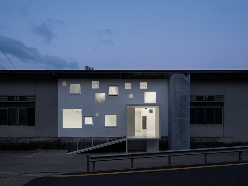 Front elevation showing irregular window openings illuminated against a dark blue evening sky