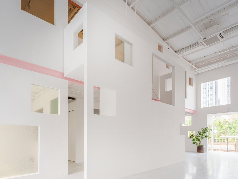 White interior partition with cut-out openings and pink steel trim beneath a sawtooth skylight