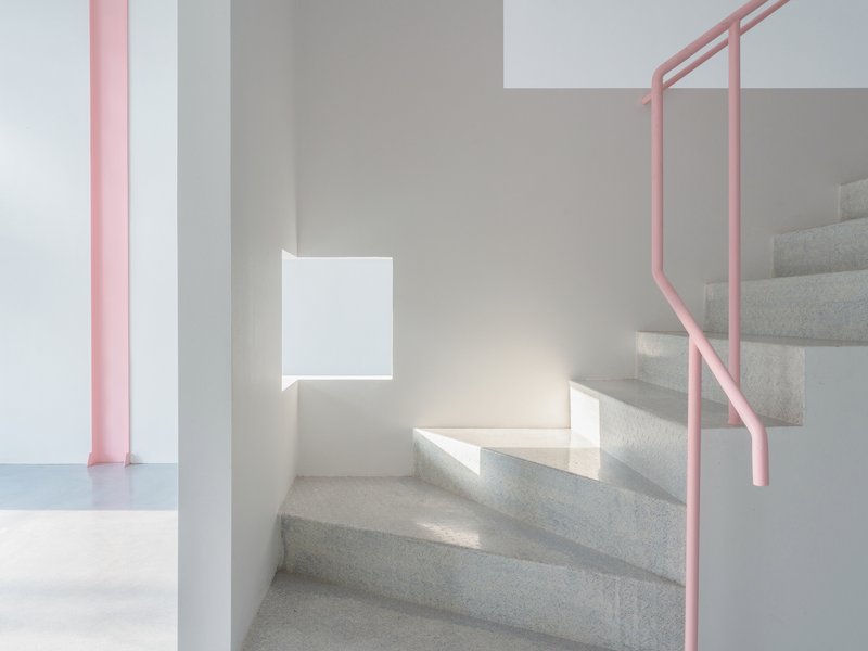 Terrazzo staircase with pink tubular handrail and sunlight casting shadows on white walls