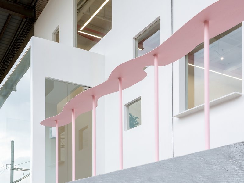 White facade with irregularly placed windows and a pink undulating canopy supported by pink columns