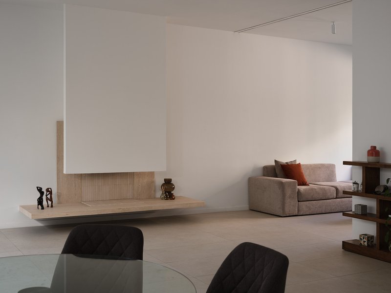Open-plan living space with floating travertine hearth, white plastered fireplace hood, and pale timber flooring