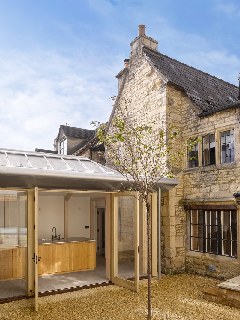 Courtyard showing the glazed extension with timber cabinetry opening onto gravel with a young tree