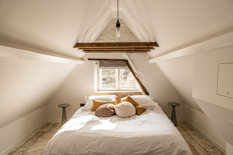 Attic bedroom with exposed timber beam and white plastered sloped ceiling lit by a dormer window