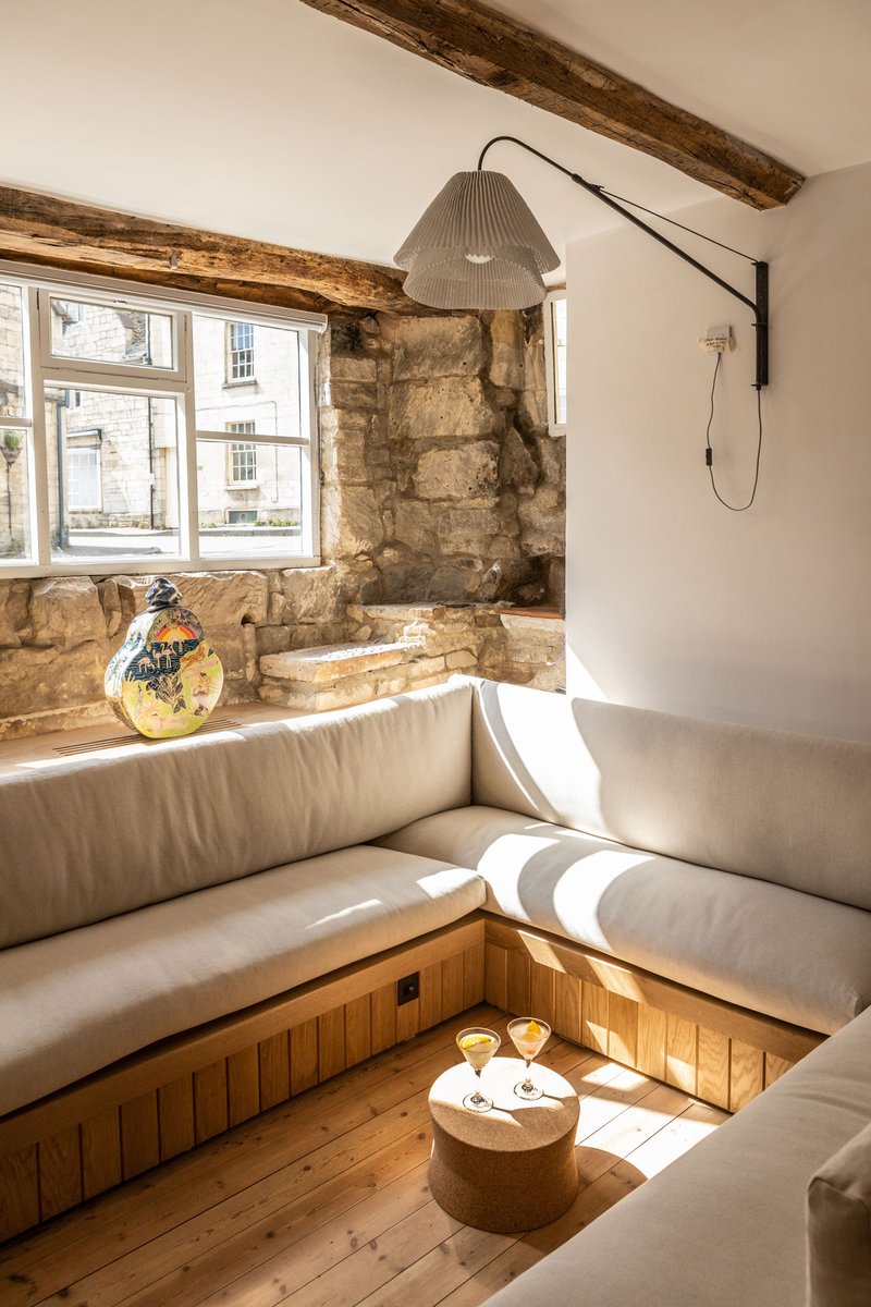 Sunken seating area with upholstered benches and exposed timber beams beside a window overlooking the street