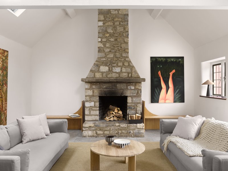 Stone fireplace with stacked firewood flanked by timber benches beneath a white vaulted ceiling with skylights