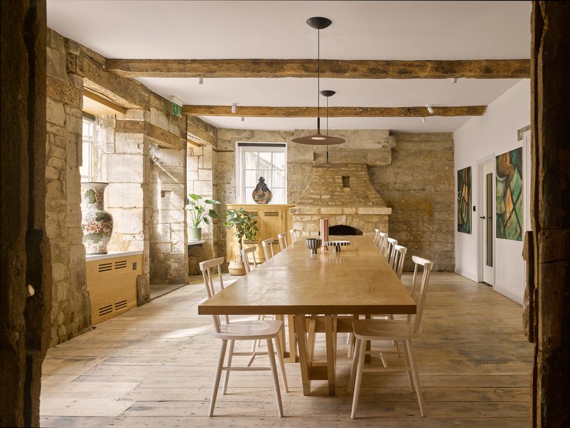 Long communal table with wooden chairs in a dining room with exposed stone walls and timber beams