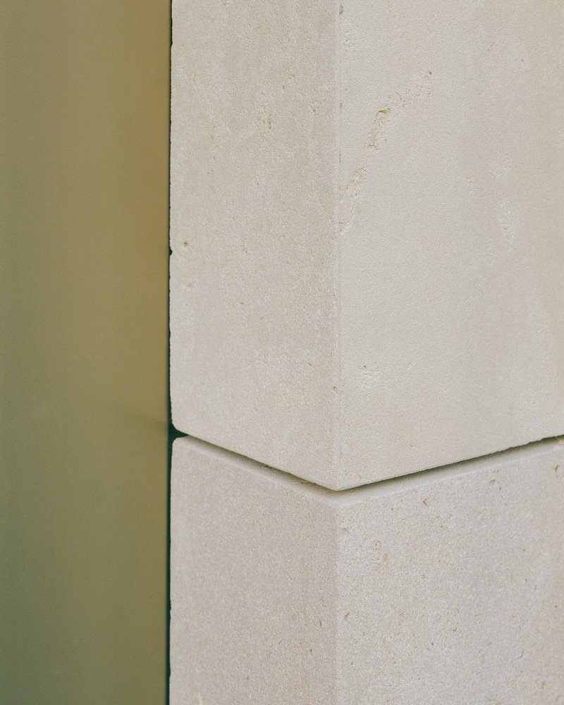 Detail of olive green metal edge meeting a pale stone panel with a chamfered joint