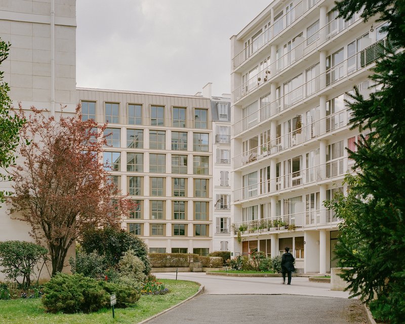 Courtyard view of the window grid facade with a figure walking the curved path in autumn