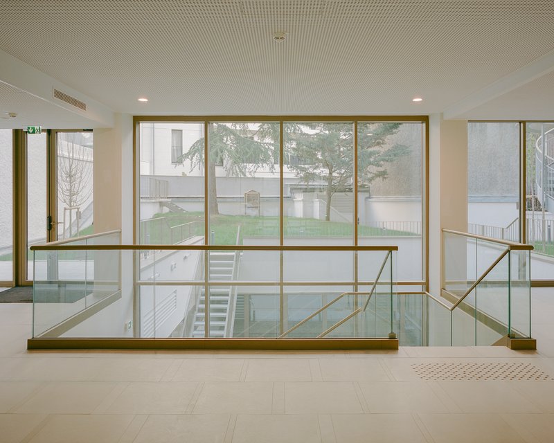 Glass and brass balustrade overlooking a courtyard garden with bare trees through floor-to-ceiling windows