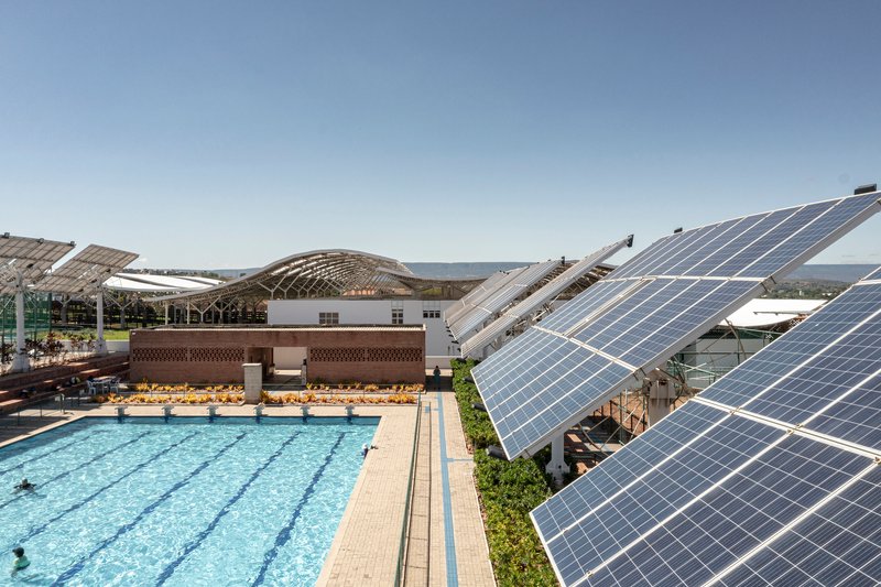 Outdoor lap pool flanked by tilted solar panel arrays and terraced seating under clear sky