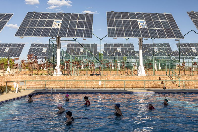 Swimming pool with children in the water backed by tracking solar panels and glass enclosure