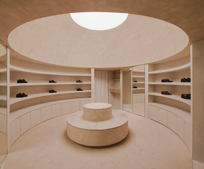 Circular retail interior with curved shelving, tiered central display plinth and circular skylight above