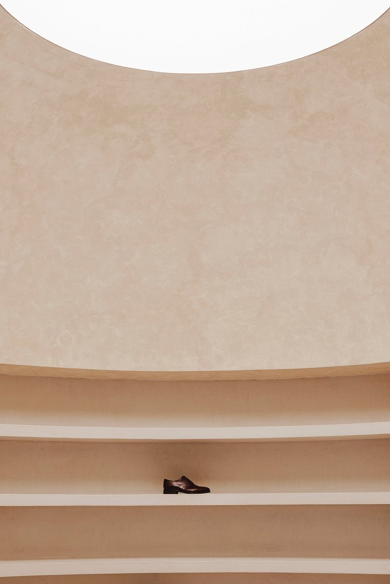 Close-up of curved plaster wall with horizontal timber shelving displaying a single shoe