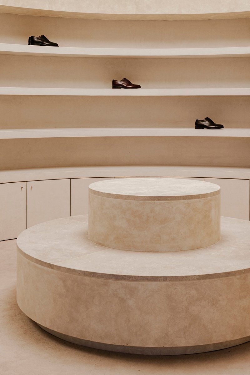 Tiered circular plinth in limestone below curved wall with shelving displaying three shoes