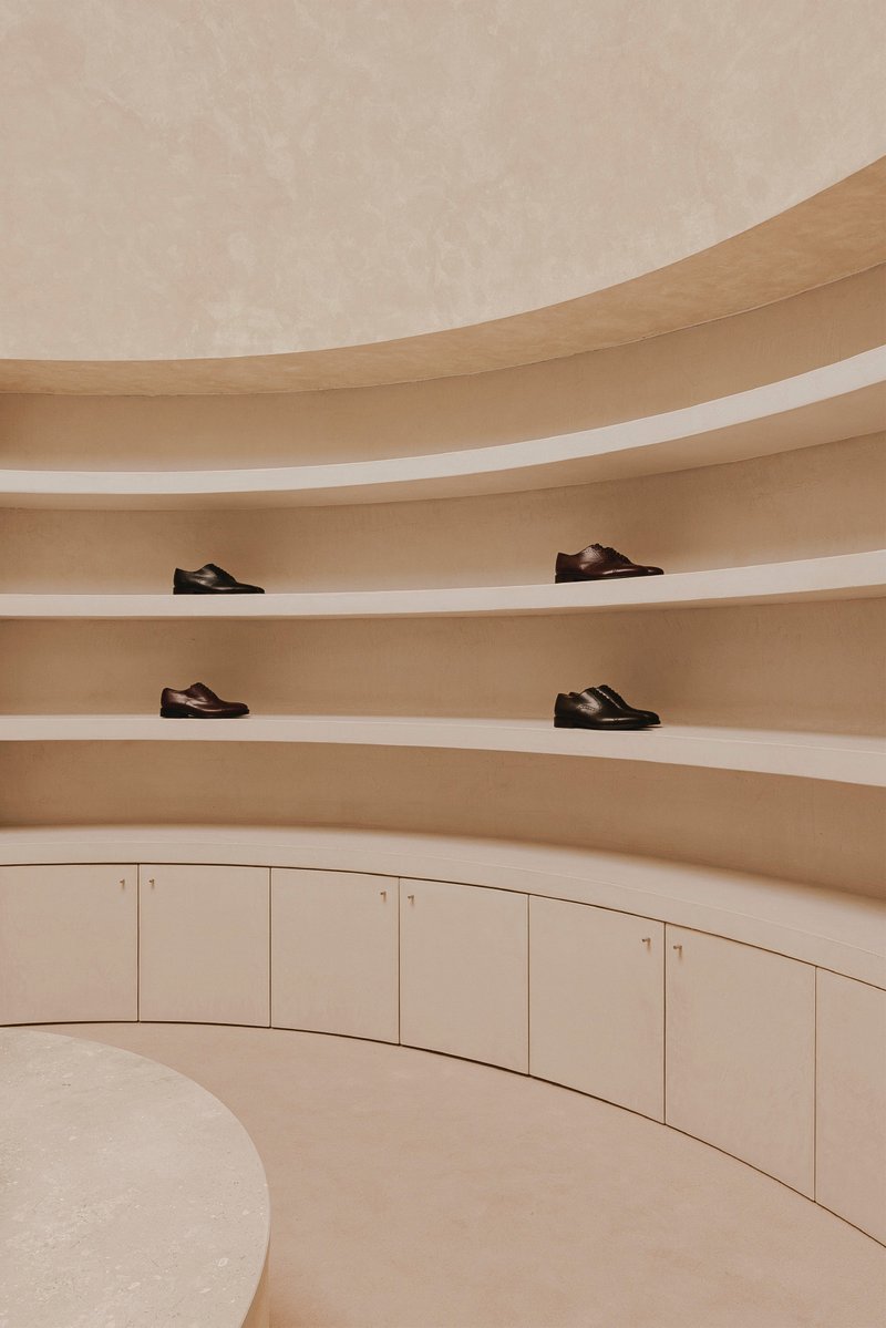 Close view of curved plywood shelving with recessed white lighting strips displaying footwear above pale storage cabinets