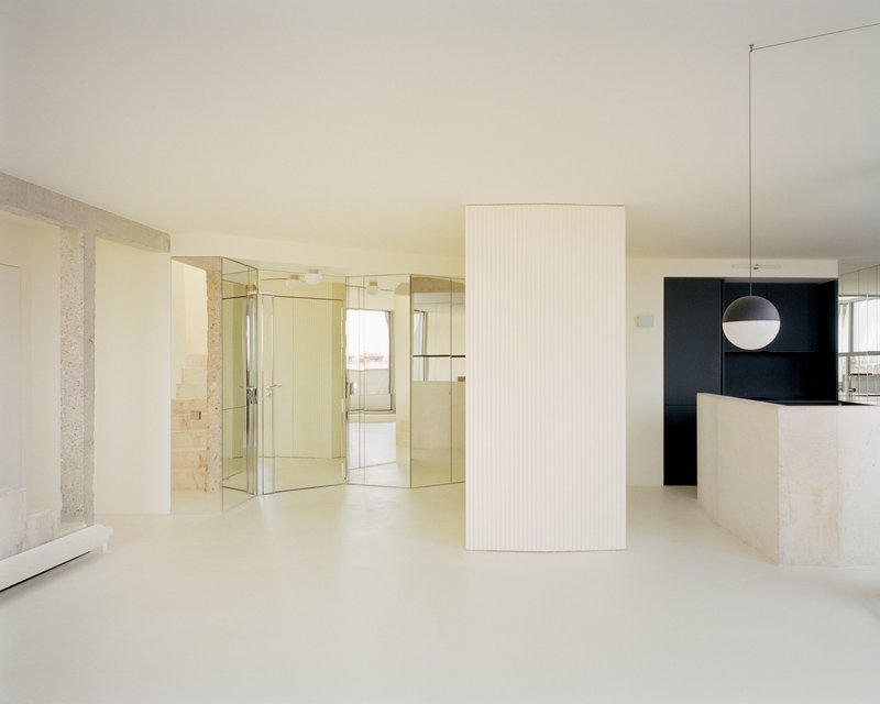 Open plan living area with fluted white volume, mirrored partition and black kitchen beyond
