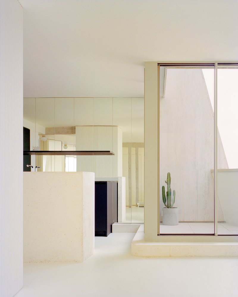 View through the kitchen island toward a glazed courtyard with a potted cactus in soft daylight