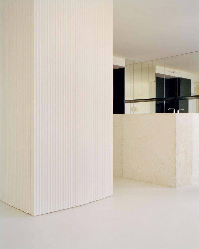 Fluted white column beside the pale stone kitchen island and mirrored upper cabinetry