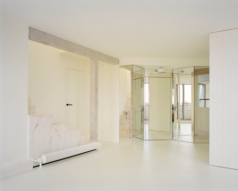 Open interior with terrazzo columns framing mirrored glass partitions and a marble-clad bench