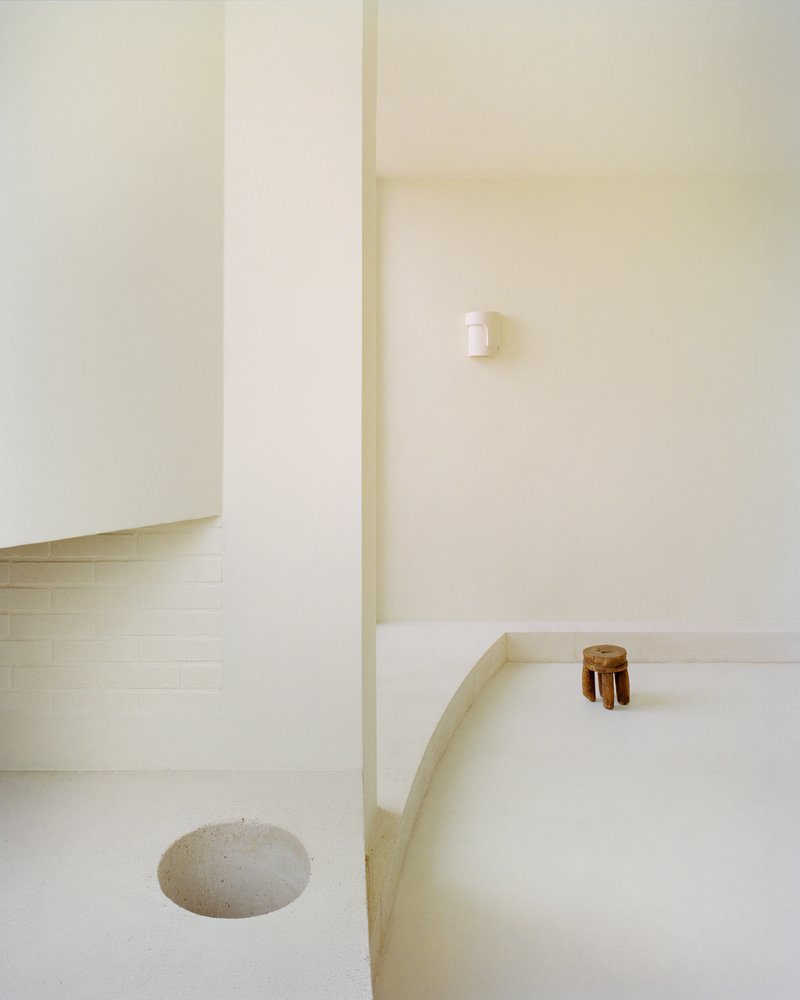 Sunken bath with pale tile surround and wooden stool beside a recessed floor drain