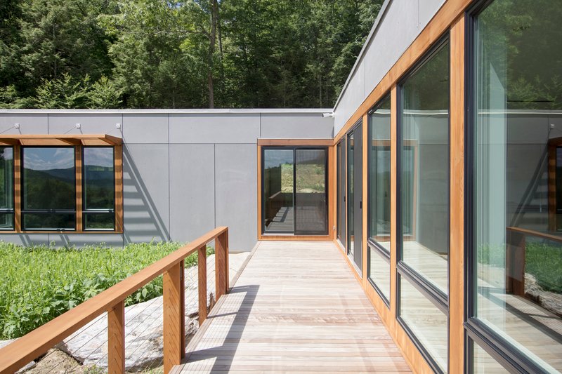 Timber boardwalk connecting glass-walled volumes with mountain views in the distance