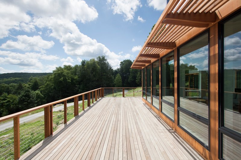 Timber deck with slatted pergola and cable railing under a blue sky with clouds
