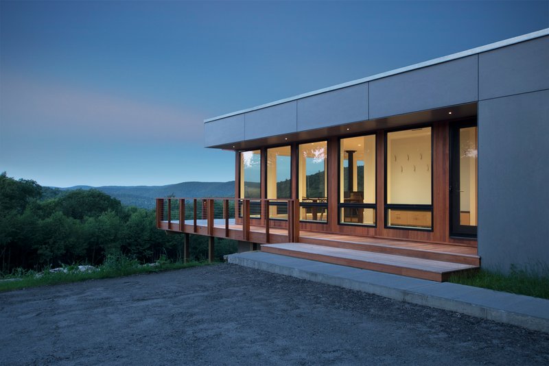 Cantilevered timber deck with vertical slat railing extending from the glazed facade at dusk